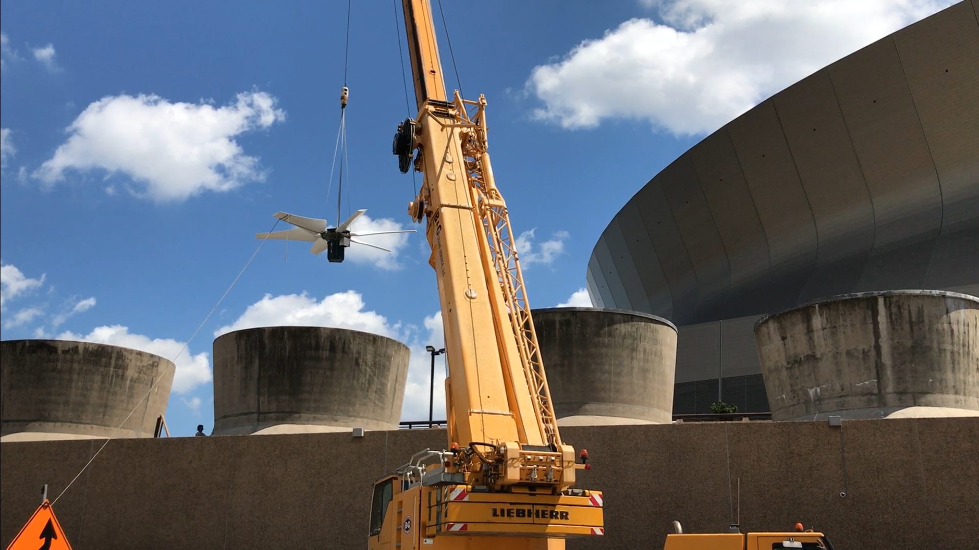 A cooling tower fan assembly suspended from a crane above the Caesars Superdome in New Orleans.